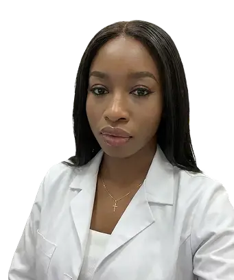 A woman with long black hair wearing a brown jacket stands confidently, showcasing her style and poise.